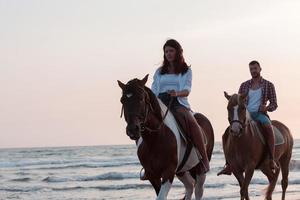 Ein liebevolles Paar in Sommerkleidung, das bei Sonnenuntergang an einem Sandstrand reitet. Meer und Sonnenuntergang im Hintergrund. selektiver Fokus foto