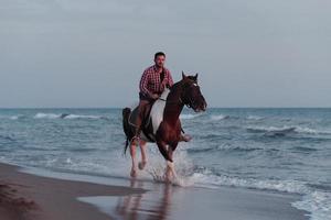 ein moderner mann in sommerkleidung genießt es, bei sonnenuntergang an einem schönen sandstrand zu reiten. selektiver Fokus foto