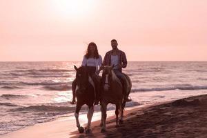 Ein liebevolles Paar in Sommerkleidung, das bei Sonnenuntergang an einem Sandstrand reitet. Meer und Sonnenuntergang im Hintergrund. selektiver Fokus foto