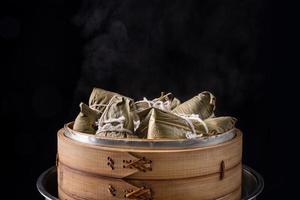 Reisknödel, Zongzi - Haufen chinesischer traditioneller gekochter Speisen auf Holztisch auf schwarzem Hintergrund, Konzept des Drachenbootfestivals, Nahaufnahme, Kopierraum