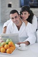 Glückliches Paar, das beim Frühstück die Zeitung in der Küche liest foto
