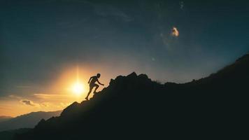 Mann klettert in einem malerischen Sonnenuntergang auf einen felsigen Bergrücken foto