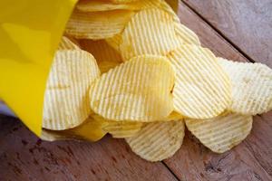 geöffnete Packung mit Kartoffelchips über Holztisch foto