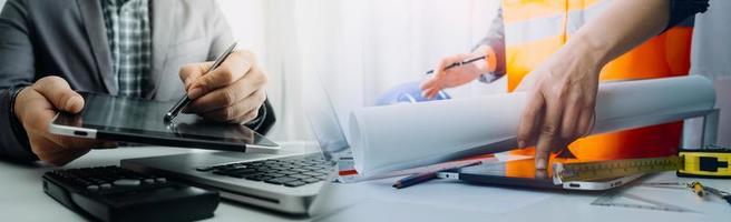 Zwei Kollegen diskutieren über Datenverarbeitung und Tablet, Laptop mit einem Architekturprojekt auf der Baustelle am Schreibtisch im Büro foto