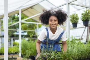 Porträt eines afrikanischen Kindes wählt Gemüse- und Kräuterpflanzen aus der Gärtnerei des örtlichen Gartencenters mit einem Einkaufswagen voller Sommerpflanzen für Wochenendgärtnerei und Outdoor-Konzept foto