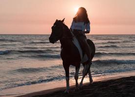 frau in sommerkleidung genießt es, bei sonnenuntergang an einem schönen sandstrand zu reiten. selektiver Fokus foto