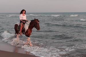 frau in sommerkleidung genießt es, bei sonnenuntergang an einem schönen sandstrand zu reiten. selektiver Fokus foto