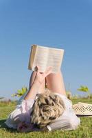 Frau, die an einem sonnigen Sommer- oder Frühlingstag auf einer mit frischem grünem Gras bedeckten Wiese liegt und ihr Lieblingsbuch liest. foto