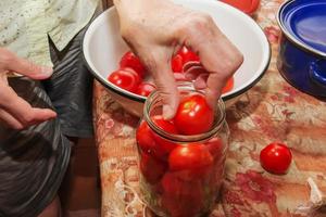 der Prozess der Konservierung von Tomaten für den Winter. weibliche hände stapeln reife rote saftige tomaten in gläsern. foto