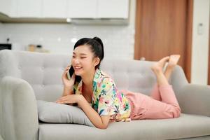 glückliche junge Frau, die mit dem Handy spricht, während sie sich auf der Couch entspannt foto