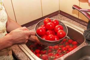 Die Hände der Frau waschen die Tomaten und entfernen die Stiele vom Gemüse. foto