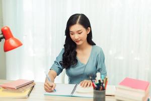 konzentrierte junge asiatische studentin, die zu hause am schreibtisch sitzt foto