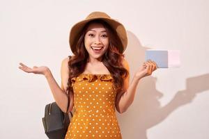 Bild einer aufgeregten brünetten Frau in den 20ern, die einen Strohhut trägt, während sie einen Pass mit Reisetickets hält, die über beigem Hintergrund isoliert sind foto