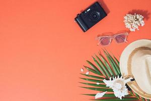 Bunte Sommerferienmode flach lag - Strohhut, Kamera, Sonnenbrille, Muscheln auf leuchtend orangefarbenem Hintergrund foto