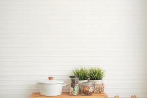Moderner weißer Küchenhintergrund minimaler Stil mit weißen Töpfen, einem Glas Kekse, einem Glas getrockneter Quittenblätter und einer Topfpflanze auf einem Holztisch. foto