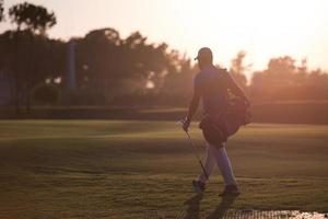 golfer, der bei schönem sonnenuntergang golftasche geht und trägt foto