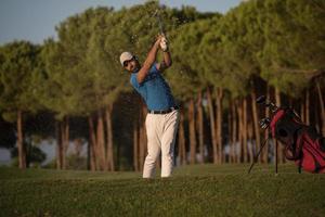 Golfspieler, der einen Sandbunker schlägt, der bei Sonnenuntergang erschossen wird foto