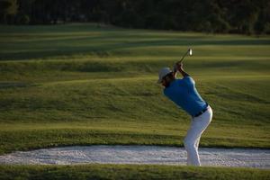 Golfspieler, der einen Sandbunker schlägt, der bei Sonnenuntergang erschossen wird foto