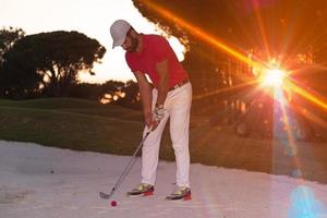 Golfspieler, der einen Sandbunker schlägt, der bei Sonnenuntergang erschossen wird foto