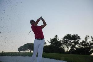 Golfspieler, der einen Sandbunker schlägt, der bei Sonnenuntergang erschossen wird foto