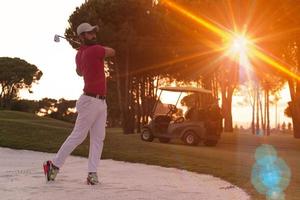 Golfspieler, der einen Sandbunker schlägt, der bei Sonnenuntergang erschossen wird foto