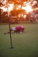 Golfspieler bläst Ball im Loch mit Sonnenuntergang im Hintergrund foto