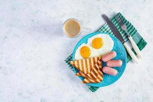 Leckeres Frühstück mit Eiern, Würstchen, Toast und einer Tasse Kaffee. amerikanisches Frühstück. Ansicht von oben