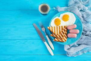 Leckeres Frühstück mit Eiern, Würstchen, Toast und einer Tasse Kaffee. amerikanisches Frühstück. Ansicht von oben