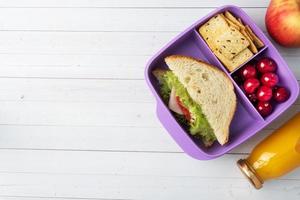 leckeres gesundes Sandwich in einer Brotdose, Keksen und Kirschen. Mittagessen mit in die Schule oder ins Büro nehmen. Saft in einer Flasche und einem Apfel. foto