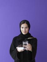 Moderne muslimische Frau in Abaya, die eine Dattelfrucht und ein Glas Wasser vor sich hält foto