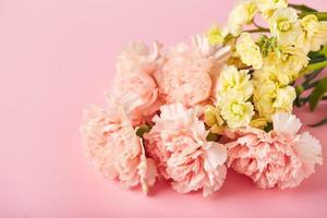 Bouquet aus rosa Nelken und gelber Matthiola. designkonzept des feiertagsgrußes mit nelkenblumenstrauß auf rosa tischhintergrund foto