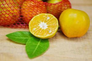 Orangenfrucht auf Holzhintergrund - frische Orangenscheibe halb und Orangenblatt gesundes Obsterntekonzept foto