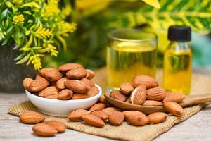 Mandelöl und Mandelnüsse auf Schalenpflanze grüner Naturhintergrund, köstliches süßes Mandelöl in Glasflaschen, geröstete Mandelnüsse für gesunde Ernährung und Snacks aus Bio-Pflanzenölen zum Kochen oder Spa foto