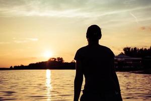 Silhouette einer Frau, die den Sonnenuntergang am Wasser genießt. foto