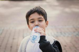 Kleiner Junge trinkt Wasser aus einer Flasche. foto
