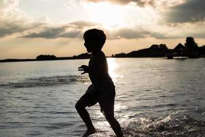 Silhouette eines Kindes, das bei Sonnenuntergang durch Wasser läuft. foto