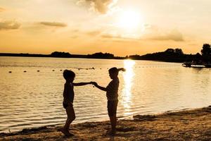 Zwei Kinder spielen bei Sonnenuntergang am Meer. foto