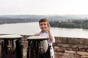 glücklicher Junge, der Conga-Instrument am Flussufer spielt. foto