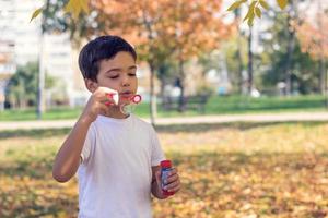 kleiner junge bläst blasen mit blasenstab im herbstpark. foto