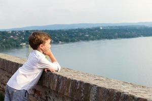 kleiner Junge genießt die Aussicht am Flussufer. foto