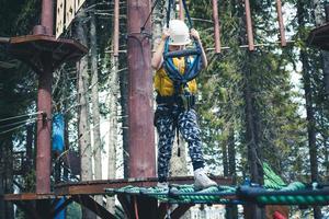 kleiner Junge, der während einer Canopy-Tour in der Natur über Hindernisse geht. foto