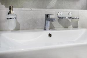 Keramik-Wasserhahn-Waschbecken mit Wasserhahn mit Seifen- und Shampoo-Spendern im teuren Loft-Badezimmer oder in der Küche foto