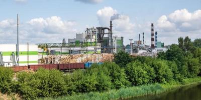 Rohre des Sägewerks des Holzbearbeitungsunternehmens in der Nähe des Flusses. Luftverschmutzungskonzept. Industrielandschaft Umweltverschmutzung Abfall von Wärmekraftwerken foto