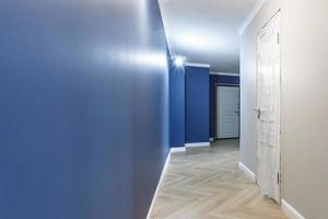 leerer unmöblierter Korridor mit minimalen vorbereitenden Reparaturen mit Zierleisten. innenraum aus weißen und blauen wänden foto