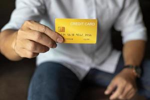 Geschäftsmann zeigt Kreditkarte, Mann sitzt zu Hause auf dem Sofa im Wohnzimmer. foto