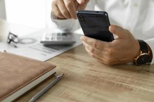 Geschäftsmann mit Telefon zur Kommunikation von Unternehmensinvestitionen, Mann im weißen Hemd, der am Schreibtisch sitzt foto