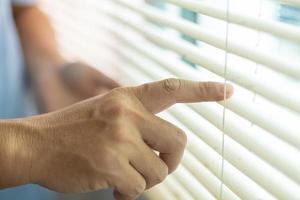 Mann, der Vorhänge überprüft, hält die Vorhänge am Fenster mit den Fingern fest. foto