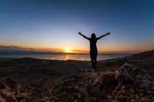 Silhouette Girl steht hoch in den Bergen, die Arme seitlich ausgestreckt und begegnet der Morgendämmerung foto