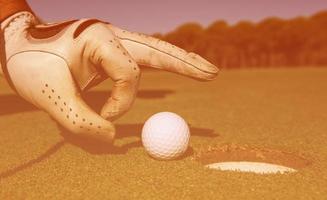 Die Hand des Mannes, die den Golfball in das Loch steckt foto