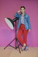 junge Frau, die sich gegen eine Studio-Taschenlampe über einem rosa Hintergrund lehnt foto